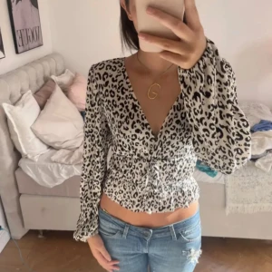 Leopardmönstrad blus - Trendig leopardmönstrad blus med v-ringning och långa ärmar. Blusen har en smickrande passform med knytning i midjan som ger en fin siluett. Perfekt för att ge en touch av djurmönster till din outfit.