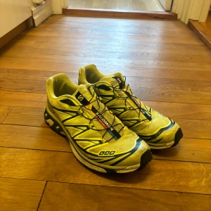 Salomon xt 6 - Säljer ett par gula Salomon löparskor med svarta och blå detaljer. Skorna har en robust sula och snörning för optimal passform. Perfekta för löpning och utomhusaktiviteter.