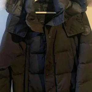 Cannada goose jacka  - Säljer en svart dunjacka med pälsdetalj på huvan. Jackan har en hög krage och knäppning med både dragkedja och knappar. Perfekt för kalla vinterdagar. Märket är cannada goose och såklart äkta, kvittot följer med. Den är i ny skick💪