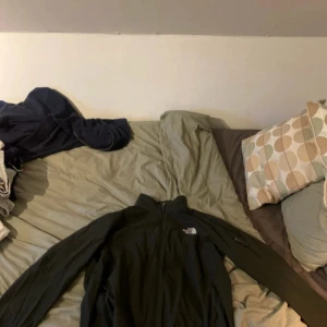 Svart jacka från The North Face - Säljer en svart jacka från The North Face med dragkedja och långärmad design. Perfekt för utomhusaktiviteter med sin funktionella stil. Jackan har en diskret logga på bröstet och är tillverkad i ett slitstarkt material.
