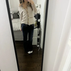 Beige och vit randig kofta - Säljer en snygg beige och vit randig kofta med guldknappar från happy holly. Koftan har långa ärmar och två fickor framtill. Super snygg och funkar att ha på många olika sätt! Skriv för frågor eller mer bilder💗