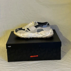 Grå sneakers från Versus Versace - Snygga grå sneakers från Versus Versace med en chunky sula och vita snören. Skorna har en modern design med olika grå nyanser och svarta detaljer. Perfekta för en stilren look. Fläckarna är bara att tvätta bort, har inget att göra rent det med.