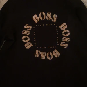 Svart tröja från Hugo Boss - Snygg svart tröja från Hugo Boss med ett unikt mönster av märkesnamnet i en cirkel på framsidan. Perfekt för en stilren look.