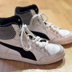 Vita sneakers med svart detalj - Snygga vita sneakers med svart detalj och gråmelerad textil upptill. Skorna har snörning och en hög krage för extra stöd. Perfekta för en avslappnad stil. Nypris: 900 kr.
