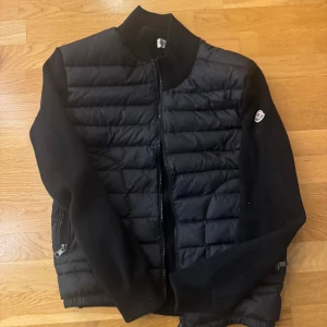 Svart pufferjacka från Moncler - Snygg svart pufferjacka från Moncler med dragkedja framtill. Jackan har långa ärmar och en quiltad design på framsidan. Perfekt för kyligare dagar.