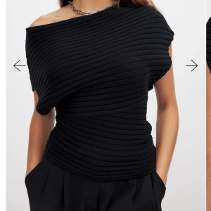 Svart ribbad offshoulder topp från NA-KD - Snygg svart ribbad topp från NA-KD med offshoulder-design. Den har en asymmetrisk form och ger en stilren look. Perfekt för att skapa en trendig outfit. Helt slutsåld överallt!!!