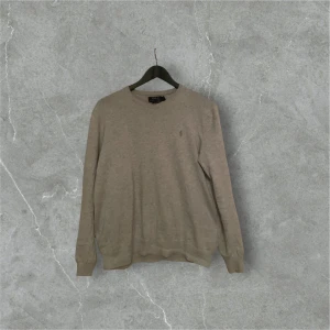 Grå tröja från Polo Ralph Lauren - Säljer en stilren grå tröja från Polo Ralph Lauren i slim fit. Tillverkad av mjuk pima bomull, perfekt för en elegant och bekväm look. Tröjan har långa ärmar och en klassisk design. Passar utmärkt för både vardag och mer uppklädda tillfällen.