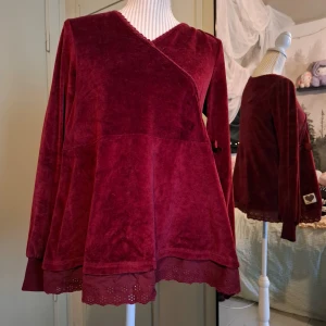Vinröd velourtröja från blooming  - Säljer en vinröd velourtröja från blooming i omlottmodell. Tröjan har långa ärmar och en dekorativ spetskant vid fållen. Perfekt för en mysig och stilren look. 💖
