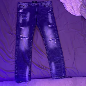 Blå jeans från Supply & Demand - Snygga blå jeans från Supply & Demand med slitna detaljer och en cool, distressed look. De har en klassisk femficksdesign och knappgylf. Perfekta för en avslappnad stil.