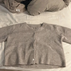 Grå ribbad kofta - Säljer en mysig beige ribbad kofta med knappar framtill. Perfekt för kyliga dagar och enkel att matcha med olika outfits. Koftan har en klassisk design med rund hals och trekvartsärmar.