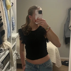 Svart ribbad topp med spetsdetaljer - Säljer en svart ribbad topp med söta spetsdetaljer på ärmarna. Den är kortärmad och gjord i ett bekvämt material. Perfekt till i sommar🌸🌺💐🌷☀️🌴