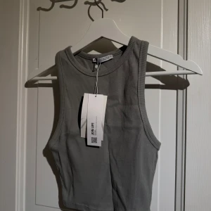 Grå ribbad linnetopp från Zara - Snygg grå ribbad linnetopp från Zara. Perfekt för en stilren look med sin ärmlösa design och croppade passform. Toppen är i mjukt material och har en rund halsringning.