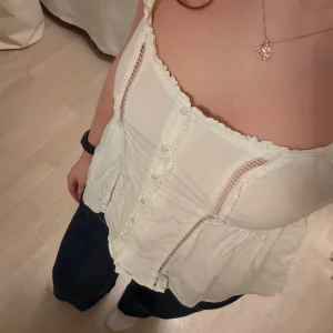 Söt topp från American Eagle Outfitters - Säljer en söt vit topp från American Eagle Outfitters med smala axelband och knappar framtill!