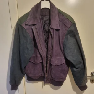 Vintage läderjacka Hunt club, colourblock - Säljer en unik vintage hun club jacka i lila,grön och blå. Jackan har en klassisk bomberstil med dragkedja och stora fickor framtill. Den har långa ärmar och en bekväm passform. Perfekt för dig som vill sticka ut med en retro look!
