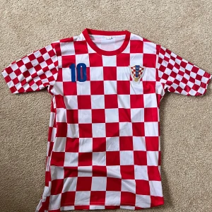 Kroatsien tröja köpt på marknad  - Snygg fotbollströja med röd och vit schackrutig design. Tröjan har korta ärmar och nummer 10 med Modric på ryggen.