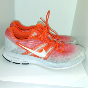 Nike löparskor i orange och vit - Säljer ett par Nike löparskor i en fräsch orange och vit färgkombination. Skorna har en luftig mesh-överdel och klassisk snörning för bra passform. Perfekta för löpning och träning.