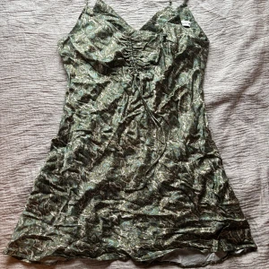 Mönstrad klänning från Zara - Snygg mönstrad klänning från Zara i gröna och beige toner. Klänningen har smala axelband och en v-ringad design med snörning framtill. Perfekt för en somrig look!