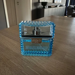 Versace Eau Fraîche Parfym - Säljer en fräsch och stilren Versace Eau Fraîche parfym i en snygg blå flaska med ett unikt mönster. Flaskan har en rektangulär form med en silverfärgad spraypump. Perfekt för den som vill ha en doft som sticker ut.