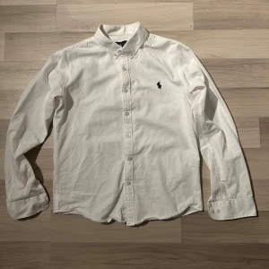 Vit skjorta från Ralph Lauren - Säljer en klassisk vit skjorta från Ralph Lauren i storlek M. Har krymt lite så sitter lite mer som S. Skjortan har långa ärmar och är dekorerad med det ikoniska broderade logotypen på bröstet. Perfekt för en stilren look. Skick är 9/5 utav 10. Bara använd lite. Tveka inte på att höra av dig!