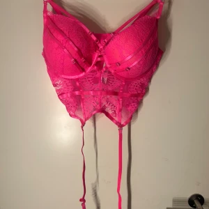 Rosa spetsbh  - Säljer en snygg rosa spetsbh med justerbara axelband och dekorativa banddetaljer. Bhn har en genomskinlig spetsdesign och knytband framtill.
