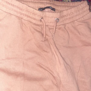 Beige mjukisbyxor med snörning - Säljer ett par bekväma beige mjukisbyxor med elastisk midja och snörning. Perfekta för en avslappnad stil. Byxorna har ribbade muddar vid bensluten för extra komfort.