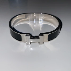 Svart armband från H-armband - Elegant svart armband från H med en stilren design. Armbandet har en metallisk H-detalj i silverfärg som fungerar som lås. Perfekt för att ge en sofistikerad touch till din stil.
