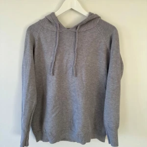 Merinoull stickad Hoodie  - Säljer en stilren grå stickad hoodie med långa ärmar och justerbar huva. Perfekt för kyliga dagar med ribbade muddar vid ärmslut och nederkant. Enkelt och snyggt plagg för en avslappnad look.