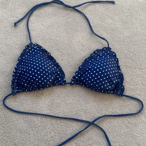 Blå prickig bikiniöverdel - Snygg blå bikiniöverdel med guldiga prickar och volangdetaljer längs kanterna. Den har knytband runt nacken och ryggen! Aldrig använd! Finns inte o köpa längre - Beck Söndergaard