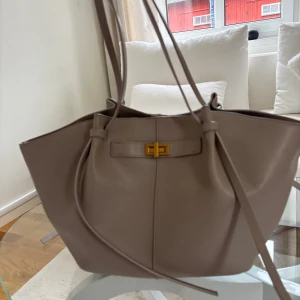 Beige axelväska med bälte - Snygg beige axelväska med stilrent bälte och gulddetaljer. Väskan har en rymlig insida med magnetlås och långa axelremmar för bekväm användning. Perfekt för att bära med sig allt man behöver under dagen. Använd några ggr 200kr