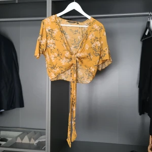 Gul blommig knytblus från Glassons - Säljer en söt gul blommig blus från Glassons med knytning framtill. Blusen har korta ärmar och ett härligt mönster i vitt och grått. Perfekt för en somrig look! 🌼 Köpt i Australien, jag gillar hur den sitter på :) 