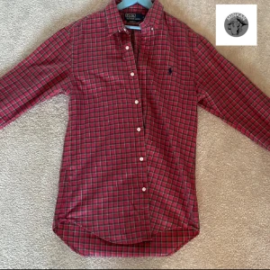 Röd rutig skjorta från Polo Ralph Lauren - Snygg röd rutig skjorta från Polo Ralph Lauren i slim fit. Skjortan har långa ärmar och knappar framtill. Den är broderad med den klassiska logotypen på bröstet. Perfekt för en stilren look.