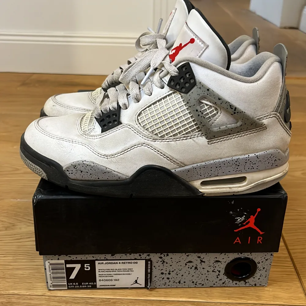 Säljer ett par klassiska Nike Air Jordan 4 Retro sneakers i vit och grå färg med svarta detaljer. Skorna har snörning och den ikoniska Jumpman-loggan i rött på plösen. Perfekta för sneakerheads som älskar retrostil.. Kengät.