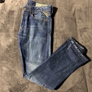 Blå jeansbyxor från replay - Snygga blå jeansbyxor från replay med klassisk femficksdesign och guldfärgade sömmar. Byxorna har en knapp och dragkedja framtill samt en läderpatch med logotyp på baksidan. Perfekta för en avslappnad stil. Storlek 32:32