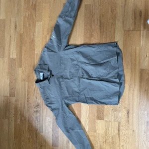 Grå skjorta från Stone Island - Snygg grå skjorta från Stone Island med diskret rutmönster och klassisk krage. Skjortan har långa ärmar och knappar framtill. Perfekt för en stilren look.