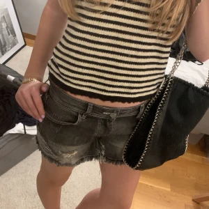 Svarta jeansshorts med slitningar - Snygga svarta jeansshorts med slitna detaljer och fransig kant. Shortsen har en klassisk femficksdesign och knappar bak. Perfekta för en avslappnad stil. !Omsydda för att få en mer låg midja!🥰storlek M men passar mig perfekt som har S