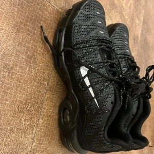 Svarta sneakers från Nike - Snygga svarta Nike sneakers med TN Air-dämpning. Skorna har ett mönstrat meshmaterial och snörning framtill. Perfekta för en sportig look.