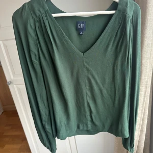 Grön blus från GAP - Snygg grön blus från GAP med v-ringning och långa ärmar. Perfekt för en stilren look. Blusen har en mjuk och bekväm passform.