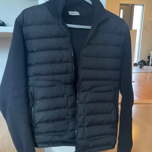  Moncler cardigan - Säljer en stilren svart cardigan från Moncler. Jackan har en dragkedja framtill och är långärmad med quiltade detaljer. Perfekt för kyligare dagar och ger en snygg look. Storlek M men passar S/M