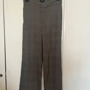 Rutiga byxor från Lindex - Snygga grå och svarta rutiga byxor från Lindex modell Lykke med hög midja och vida ben. Perfekta för en stilren look. Byxorna har en dragkedja och knappar framtill för enkel stängning. Aldrig använda! 