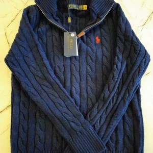 Mörkblå stickad tröja från Polo Ralph Lauren - Säljer en snygg mörkblå stickad tröja från Polo Ralph Lauren med dragkedja och ribbad krage. Tröjan har ett klassiskt flätmönster och den ikoniska röda loggan på bröstet. Perfekt för kyliga dagar! Pris kan diskuteras 