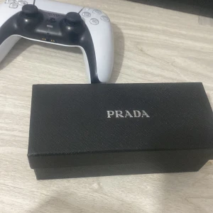 Svarta solglasögon från Prada - Snygga svarta solglasögon från Prada med en stilren design. Glasögonen kommer i ett elegant fodral och med ett äkthetscertifikat. Perfekta för att ge din outfit en lyxig touch.