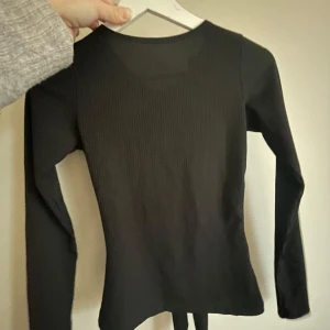 Svart ribbad topp med knyt - Svart ribbad topp med lång ärm och öppen rygg med knytning. 