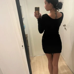 Svart sammet klänning - Snygg svart klänning i sammet med långärmad design. Den har en tight passform och kort längd, perfekt för en elegant look. Klänningen är stilren och passar bra till olika tillfällen.