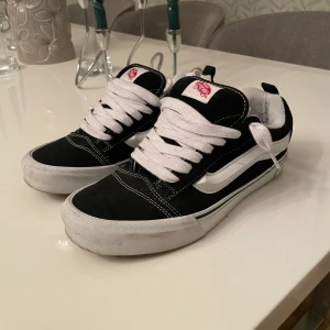 Vans Knu skol - Säljer ett par klassiska Vans sneakers i svart och vitt med vit sula och snörning. Perfekta för en avslappnad stil.