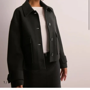 Svart jacka med knappar - Snygg svart jacka med knappar framtill och stora fickor. Den har en klassisk krage och långa ärmar med justerbara manschetter. Perfekt för en stilren look.