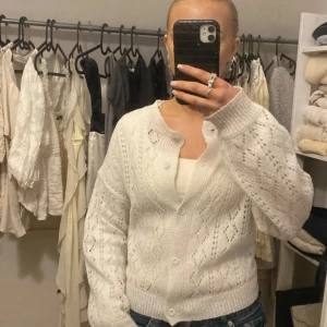 Vit stickad kofta - Säljer en mysig vit stickad kofta med knappar. Koftan har ett fint hålmönster och långa ärmar, perfekt för kyliga dagar. Passar bra till jeans eller kjol.