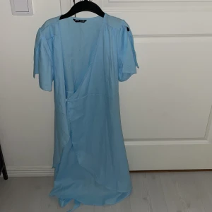 Ljusblå omlottklänning - Snygg ljusblå omlottklänning med kortärmad design och v-ringad hals. Perfekt för sommarens varma dagar.