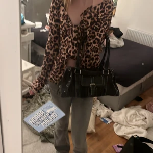 Svart axelväska med spänne - Snygg svart axelväska med vita sömmar och ett dekorativt spänne framtill. Väskan har dubbla handtag och detaljer i metall. Perfekt för att ge en stilren touch till din outfit. Väldigt rymlig!! Har många fack