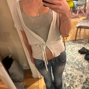 Grå glittrig kofta från Vero Moda - Säljer en grå glittrig kofta/bolero från Vero Moda. Den har korta ärmar och ett knyte runt midjan. Använd en gång!