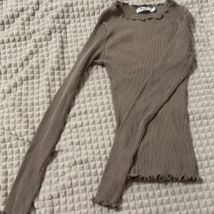 Beige ribbad tropp - Säljer en stilren beige ribbad tröja har långa ärmar och en fin volangdetalj vid hals och nederkant. Perfekt för lager-på-lager under kyligare dagar. Om ni vill se den på, skriv gärna!